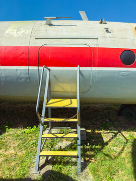 Old airplane fuselage at an outdoor location with yellow steps leading up to a door during bright daylight hours