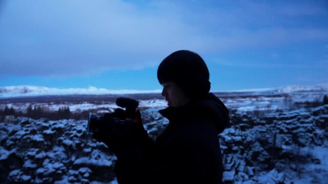 アイスランドの雪原でカメラを構える旅行者のシルエット、薄明の溶岩台地（Iceland Winter Landscape Photographer Silhouette at Dusk）