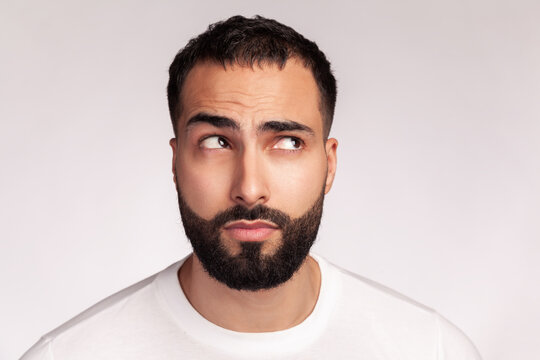 Bearded handsome man frowning face for skin elasticity and wrinkles examination looking away wearing white t-shirt isolated over gray background