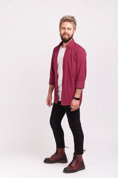 Proud young man with beard blond dyed hair wearing red checkered shirt standing with bold steady look masculine confidence isolated over gray background