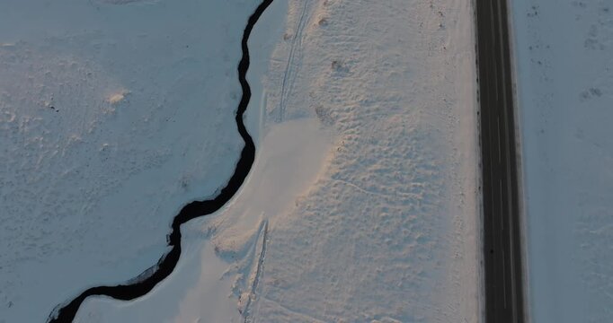 アイスランドの雪原を蛇行する黒い川と一本道を真上から空撮（Iceland Snow Field Winding River Aerial）