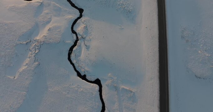 アイスランドの雪原を蛇行する川と一本道を真上から空撮（Aerial Top Down of Winding River and Road in Snowy Iceland）