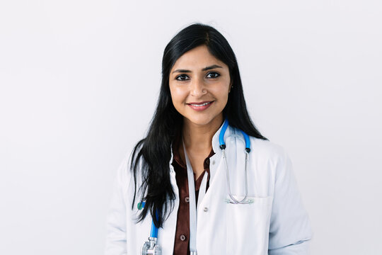 Close up portrait of smiling Indian female doctor with arms crossed on white background. Friendly healthcare professional wearing stethoscope. Healthcare and medicine concept.