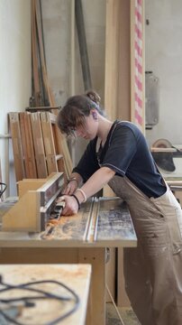 Skilled focused craftswoman processing wooden board on router machine in restoration woodshop, female carpenter carefully adjusting and shaping timber on electric instrument, removing wood layers.
