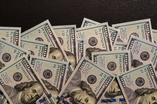 Scattered one hundred US dollar bills heap on dark background, closeup. High angle flat lay view of large pile of Benjamin Franklin 100 USD banknotes messy spread across black textured surface