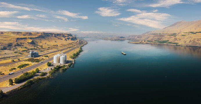 Aerial view of the Columbia River Gorge featuring industrial grain silos, a highway, and a barge on the water in Columbia River Gorge, OR, United States.
