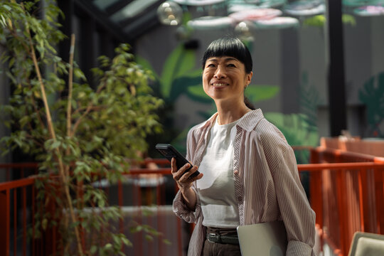 Smiling asian woman holding smartphone and laptop looking up