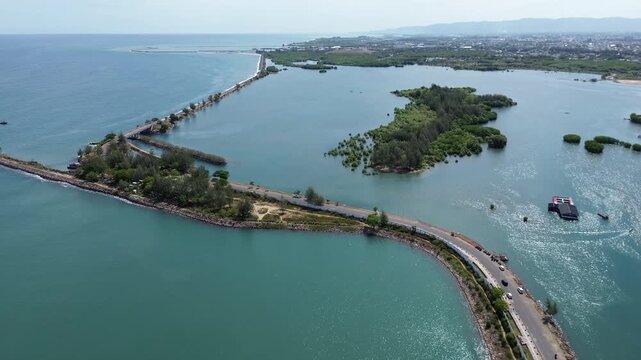 An aerial drone view of the coastal road in Ulee Lheue, Banda Aceh, leading towards the ferry port to Sabang Island, surrounded by calm sea waters and mountains.