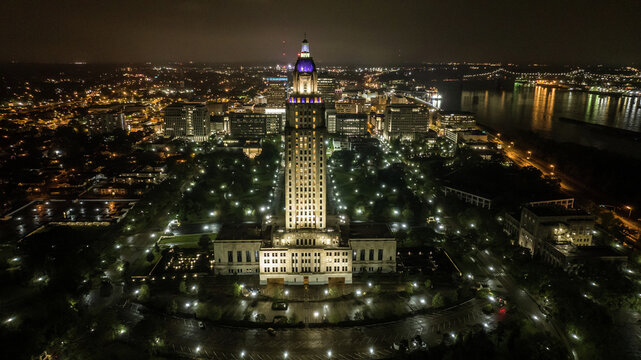 Aerial view of the illuminated Louisiana State Capitol building at night surrounded by the city lights and the Mississippi River in Baton Rouge, Louisiana, United States.