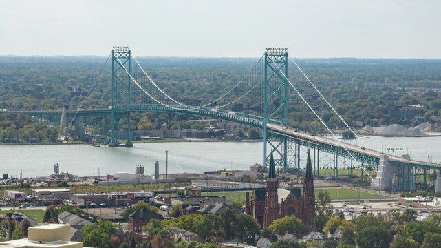 Aerial view of the Ambassador Bridge spanning the Detroit River with urban infrastructure and a historic church in the foreground in Windsor, Ontario, Canada.