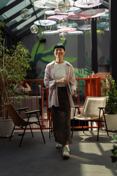 Asian woman walking in modern creative workspace holding tablet