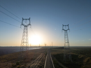Naklejka premium high voltage power transmission towers and road landscape at sunset