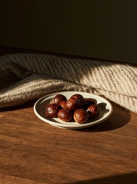 Plate of chestnuts on a wooden table. the plate is white and round, and the chestnuts are dark brown in color.