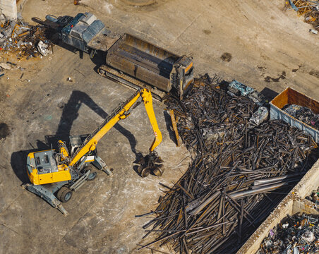 Aerial view of scrap metal recycling yard with an industrial material handler sorting steel waste and heavy machinery at a waste processing facility Le Pouzin, Auvergne-Rhone-Alpes, France.