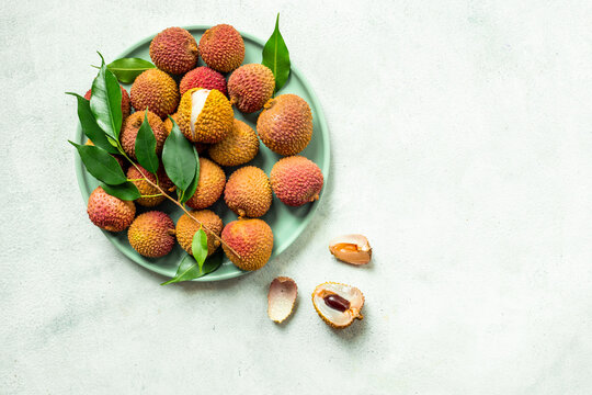 Fresh lychee fruit with green leaves on a plate, top view