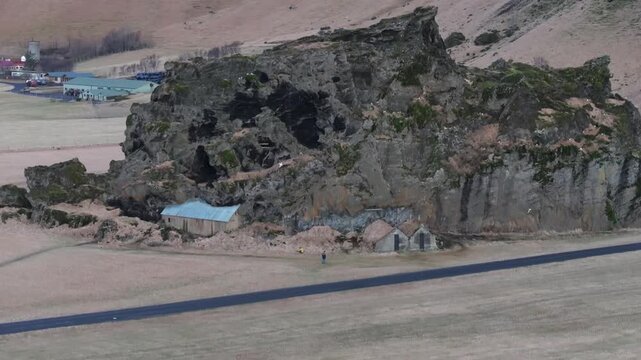 アイスランドの断崖にたたずむ古い農家の家屋を空撮（Iceland Aerial Old Farmhouses Beneath Rocky Cliff）