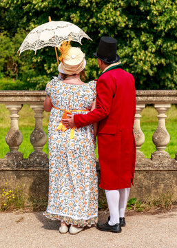 A couple dressed in Regency-era historical costumes stands together, enjoying a stroll in a garden, reflecting the elegance and romantic atmosphere of the 19th century.