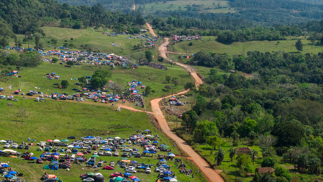 Aerial view of Rally Paraguay with numerous spectators camping and parked cars along a winding dirt road in the rural landscape of Nueva Alborada, Itapua Department, Paraguay.
