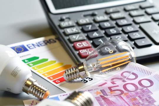Calculating electricity bill costs with calculator, EU energy efficiency label, filament light bulb and Euro banknotes