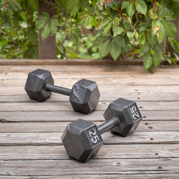 a pair of heavy cast iron hex dumbbells on a weathered wooden deck - backyard fitness concept