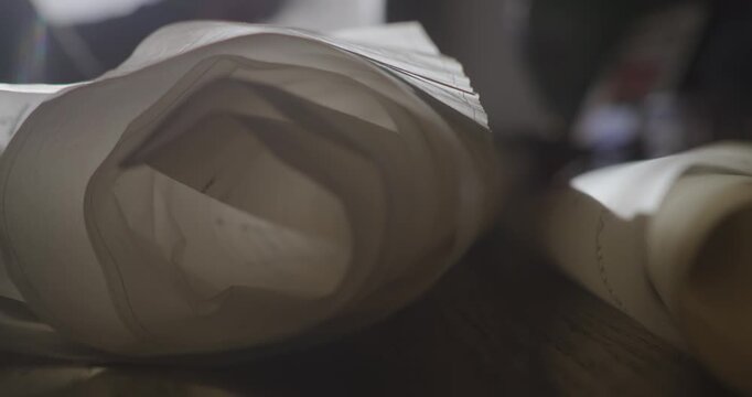 Side-profile close-up shows a person examining long scrolls of paper before removing them from a table, suggesting archival research, records or planning.