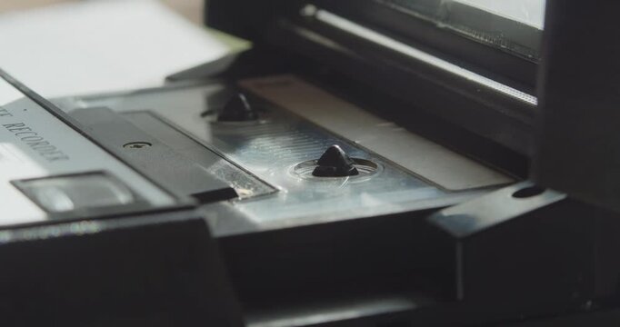 Macro close-up shows a hand inserting a cassette tape into a portable retro machine, illustrating hands-on use of vintage analog audio equipment.