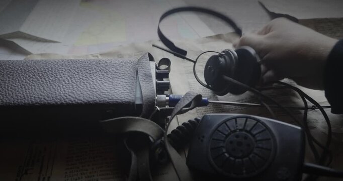 Close-up radio operator tunes a walkie talkie while listening through a headset, evoking military communications, surveillance and intelligence gathering.