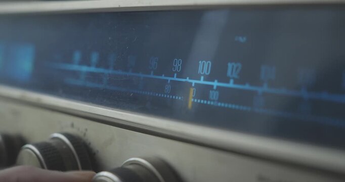 Close-up shows a hand adjusting the radio frequency dial on a retro home stereo system, illustrating analogue tuning and vintage audio technology.