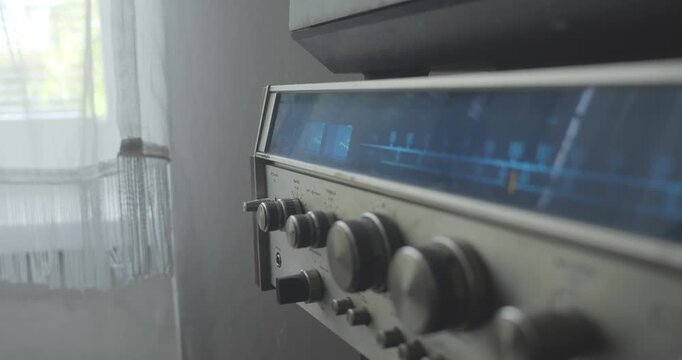 Side-profile close-up shows a retro stereo radio frequency display illuminating blue as a hand activates the system, evoking analogue home entertainment technology.