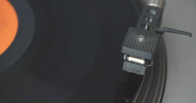 Close-up shows a record turntable spinning before the tonearm moves and lowers its stylus onto a vinyl LP, illustrating retro analogue playback technology.