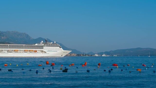 Large cruise ship sailing on the blue sea. Majestic white cruise liner sailing slowly across a calm blue sea, passing by colorful buoys with distant mountains and a coastal town visible on the horizon