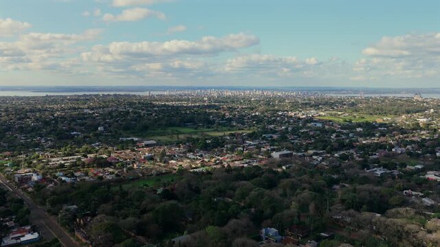 Wide aerial panorama reveals residential neighborhoods extending toward the distant skyline of Posadas, Argentina.