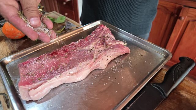 Close Up of Hand Seasoning Raw Pork Ribs with Salt for Cooking in a Home Kitchen