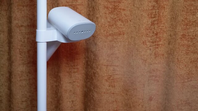 Garment steamer emitting hot steam for clothes. Modern white garment steamer releasing hot vapor to smooth out wrinkles on clothing. Essential household appliance for laundry care, ironing