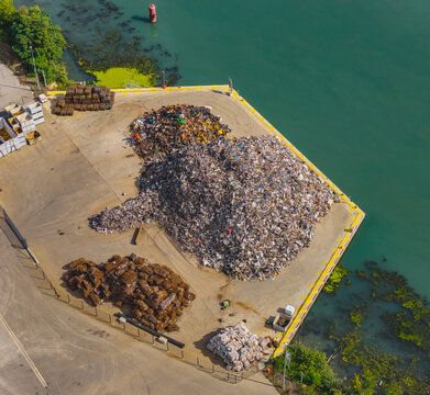 Aerial view of massive piles of scrap metal at a recycling facility beside a river, showing industrial waste recovery and circular economy efforts in Le Pouzin, Auvergne-Rhone-Alpes, France.