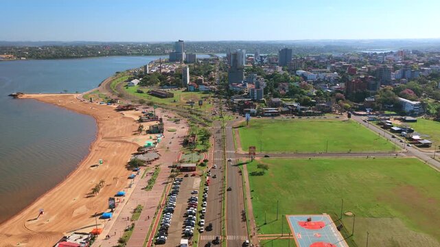 Playa San Jose borders the Parana River along Costanera Republica del Paraguay in Encarnacion, Itapua, with sandy beach, green recreation areas and sports facilities, drone forward flyover.