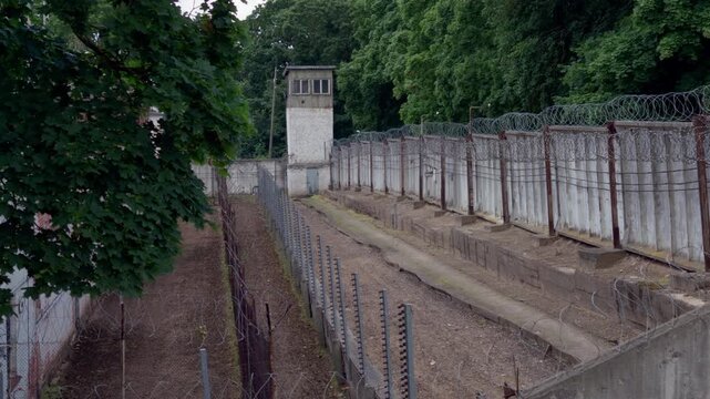 High angle perspective looking along fortified security zone with rows of barbed wire fencing and guard observation tower at Daugavpils prison in Latvia.