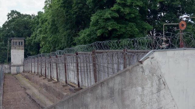 Wide camera panning movement showing concrete wall corner fitted with light fixture and coiled security wire at historic prison facility in Daugavpils city.