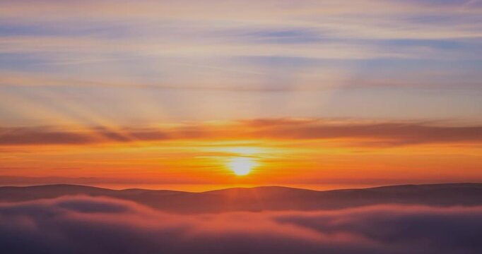 Sunset rays shining through clouds over misty hills.
