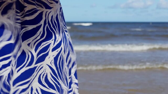 Close up view of elegant blue and white patterned dress moving in ocean breeze with soft breaking waves in background on Jurmala beach coast in Latvia.