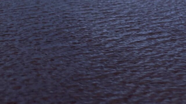 Close up view of shallow rippling water moving over wet sand during evening twilight on Baltic sea coast, creating tranquil abstract fluid motion pattern.