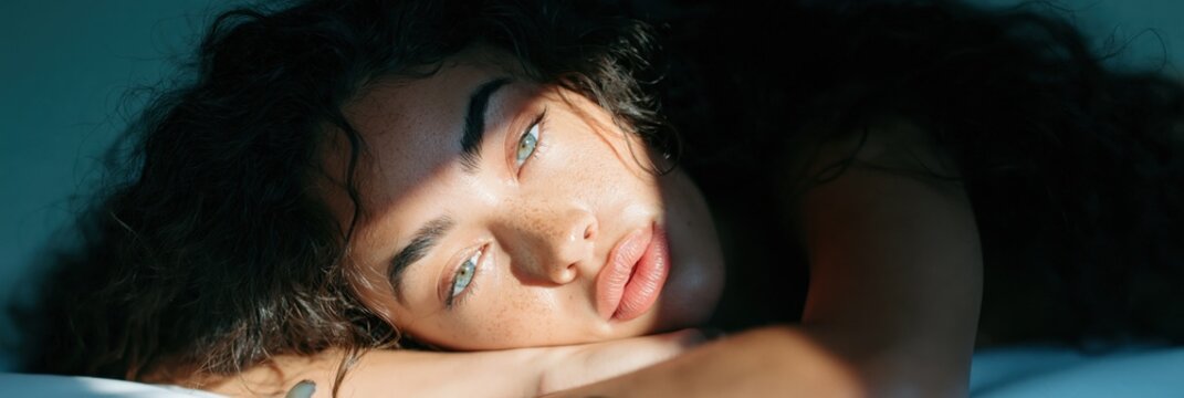 Horizontal intimate portrait of a woman lying in warm sunlight with deep shadows for lifestyle background and beauty layout