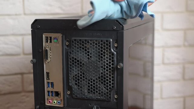 Computer technician cleaning a dusty pc case. Unrecognizable technician performing maintenance, carefully cleaning the dust from the back panel of a black desktop computer tower with a microfiber
