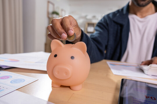Piggy bank saving coin on home office desk with financial papers and tablet, expressing careful money management and personal finance planning for household budgeting