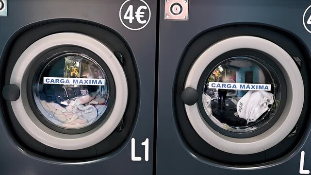 Footage of coin operated washing machines running with clothes tumbling inside at a self service laundromat in Spain a scene of everyday laundry chores in a launderette.