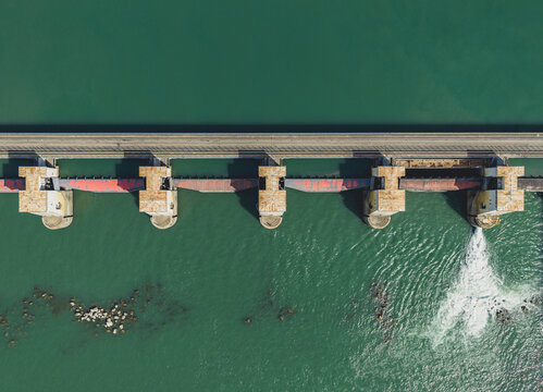 Aerial view of a river dam featuring multiple sluice gates and hydraulic engineering infrastructure regulating water flow in Le Pouzin, Auvergne-Rhone-Alpes, France.