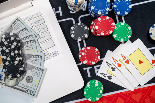 Top View of Four Aces Poker Cards near Hundred Dollar Cash Fan Laptop and Color Casino Tokens