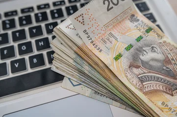 Stack of Polish Zloty Banknotes on White Laptop Keyboard for E Commerce and Online Earnings © RomanR