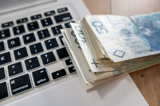 Close up of Polish Money Cash Bills Stacked on White Laptop Keyboard for Digital Banking Concept