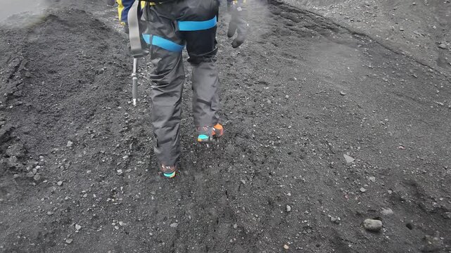 アイスランドの氷河トレッキング、火山灰に覆われた氷河上をアイゼンで歩く登山者の足元（Iceland Glacier Hiking with Crampons on Ash-Covered Ice）